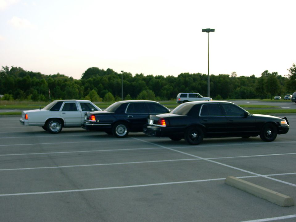 Three older sedans parked in a lot at dusk; white wagon and two dark sedans