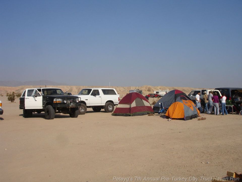 Two modified SUVs and a pickup truck parked in a desert with tents set up