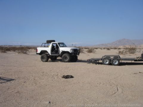 1994 Ford Bronco - A modified SUV with its doors open is parked in a desert, attached to a dual-axle trailer.