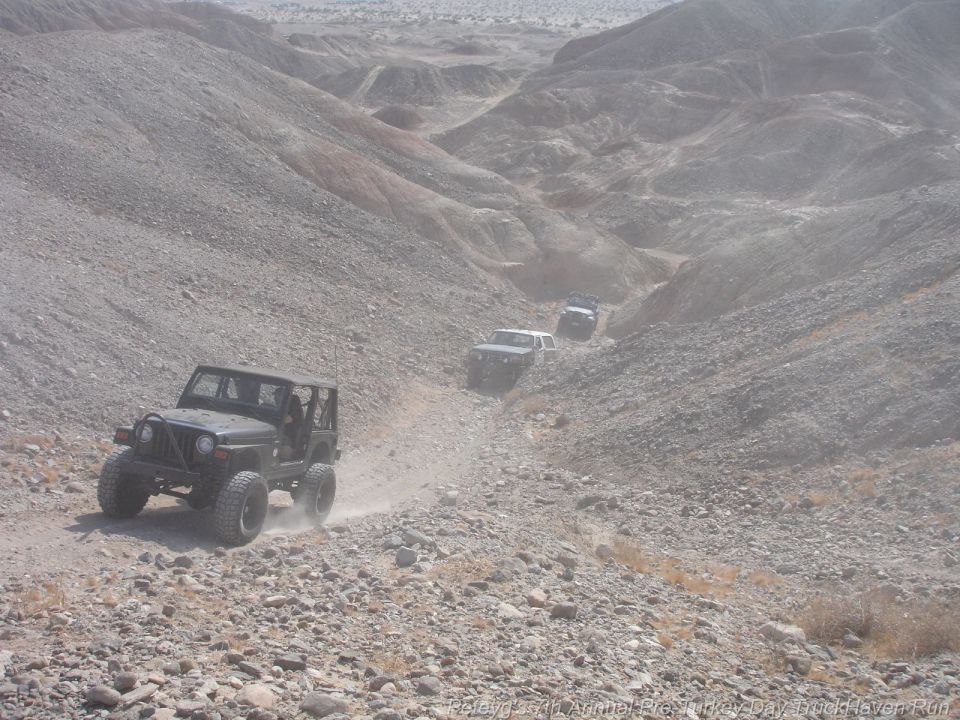 Black Jeep Wrangler driving on a rocky desert trail with other vehicles behind