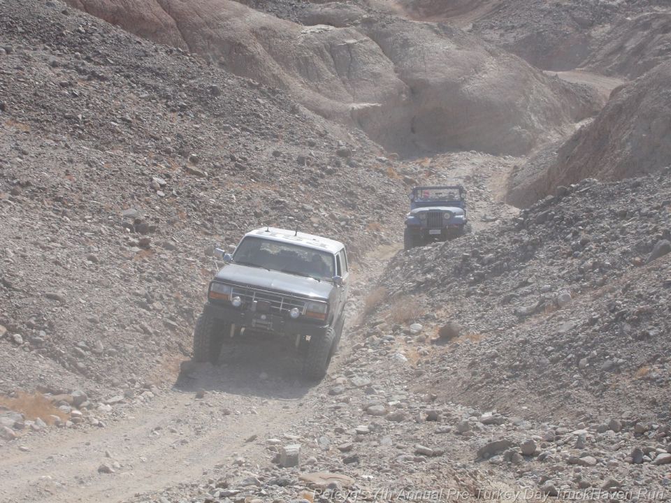 1994 Ford Bronco and a Jeep driving up a dusty, rocky canyon trail