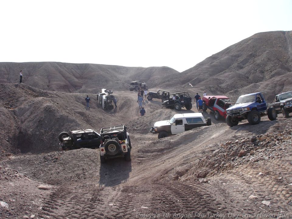 Several off-road vehicles navigating a dusty, hilly terrain. One vehicle is overturned