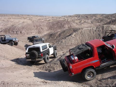 1994 Ford Bronco - A two-tone Ford Bronco navigates a desert trail alongside other off-road vehicles.
