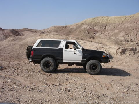 1994 Ford Bronco - 1994 Ford Bronco in a desert setting, equipped for off-road use with large tires and a spare tire on the back.
