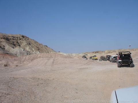 1994 Ford Bronco - A convoy of off-road vehicles navigates a dusty, arid terrain under a clear blue sky.
