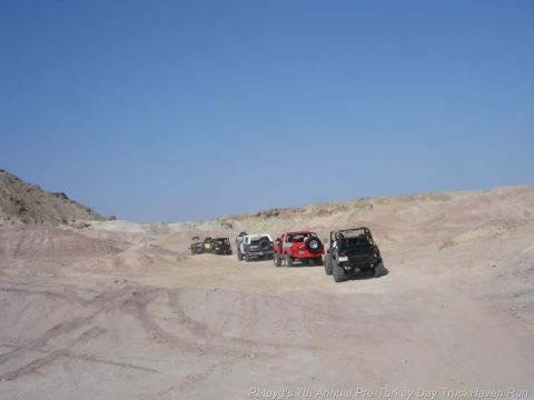 1994 Ford Bronco - A convoy of off-road vehicles, including a 1994 Ford Bronco, navigates a desert landscape under a clear blue sky.