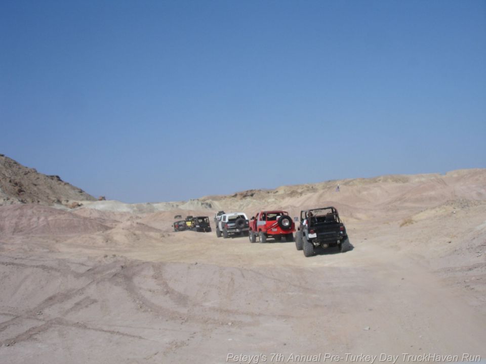 Four-door 1994 Ford Bronco in black, red, and white, driving on a dirt trail with rocky hills in the background