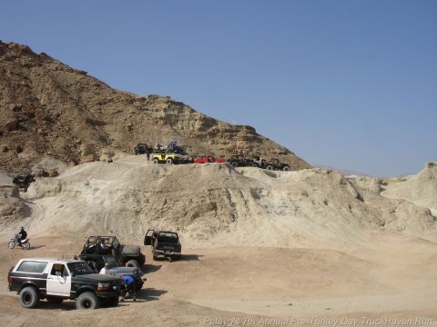 1994 Ford Bronco - A two-tone Ford Bronco is parked on the dirt, with several other off-road vehicles visible in the desert landscape.