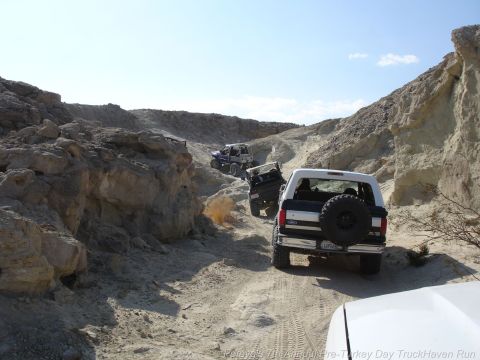 1994 Ford Bronco - A convoy of SUVs, including a white 1994 Ford Bronco, navigates a dusty, rocky trail under a clear blue sky.