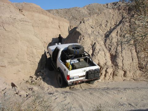 1994 Ford Bronco - This 1994 Ford Bronco is shown off-roading through a tight, sandy canyon with a spare tire mounted on its roof rack.