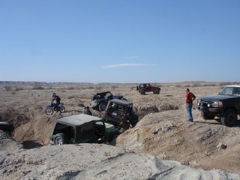 1994 Ford Bronco - Several off-road vehicles navigate a challenging desert terrain under a clear blue sky.