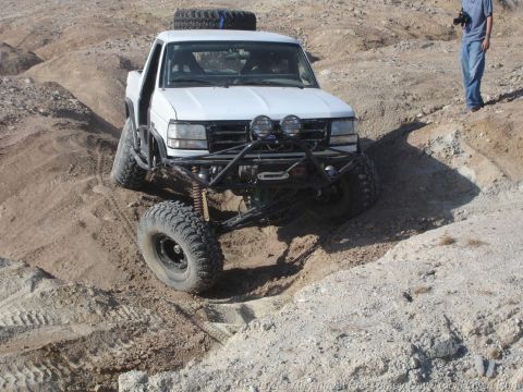 1994 Ford Bronco - A heavily modified pickup truck navigates a steep, sandy incline in an off-road environment.