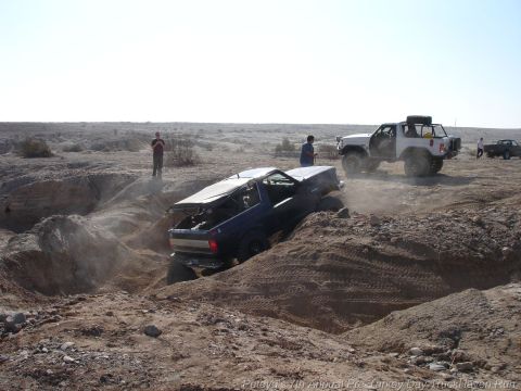 1994 Ford Bronco - Multiple off-road vehicles navigate a challenging desert terrain with one SUV stuck in a deep rut.