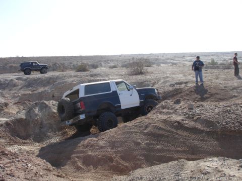 1994 Ford Bronco - A two-tone SUV tackles a challenging off-road course, with another vehicle visible in the background.