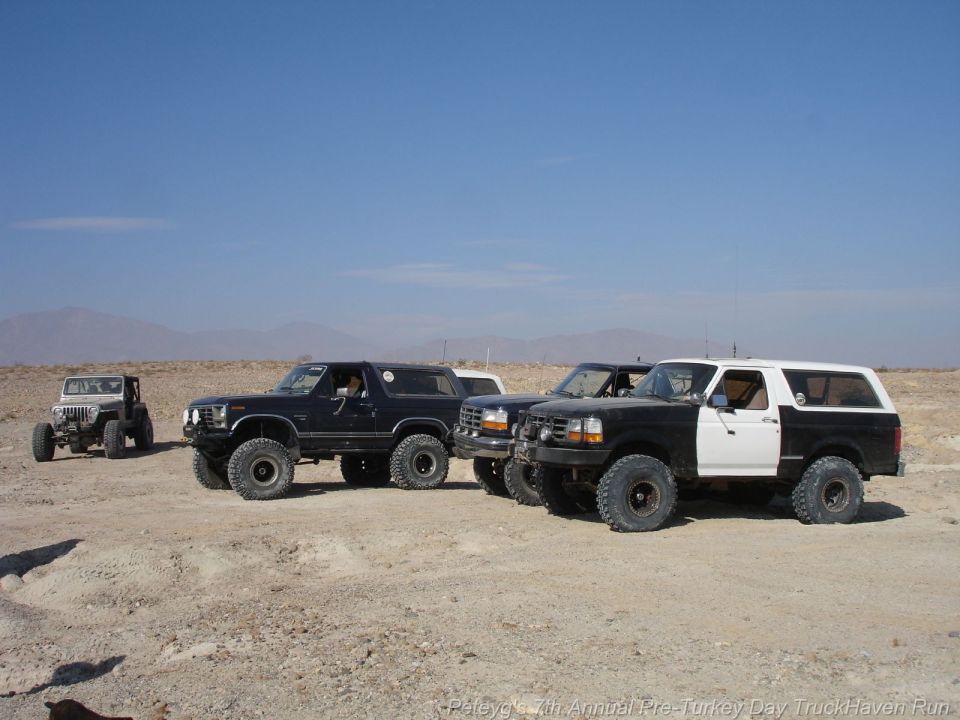 Three Ford Broncos and one Jeep Wrangler parked in a desert landscape