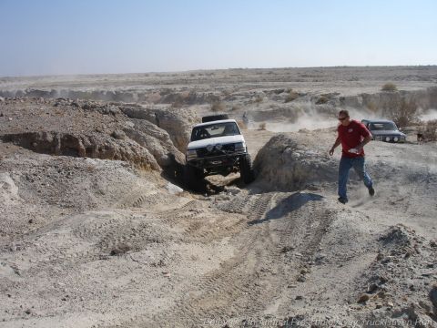 1994 Ford Bronco - Two trucks traverse a dusty, rocky canyon during an off-road event.