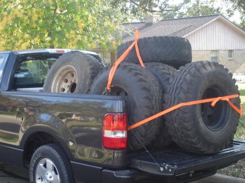1996 Ford F-150 - Pickup truck bed carries multiple large tires strapped down for transport.