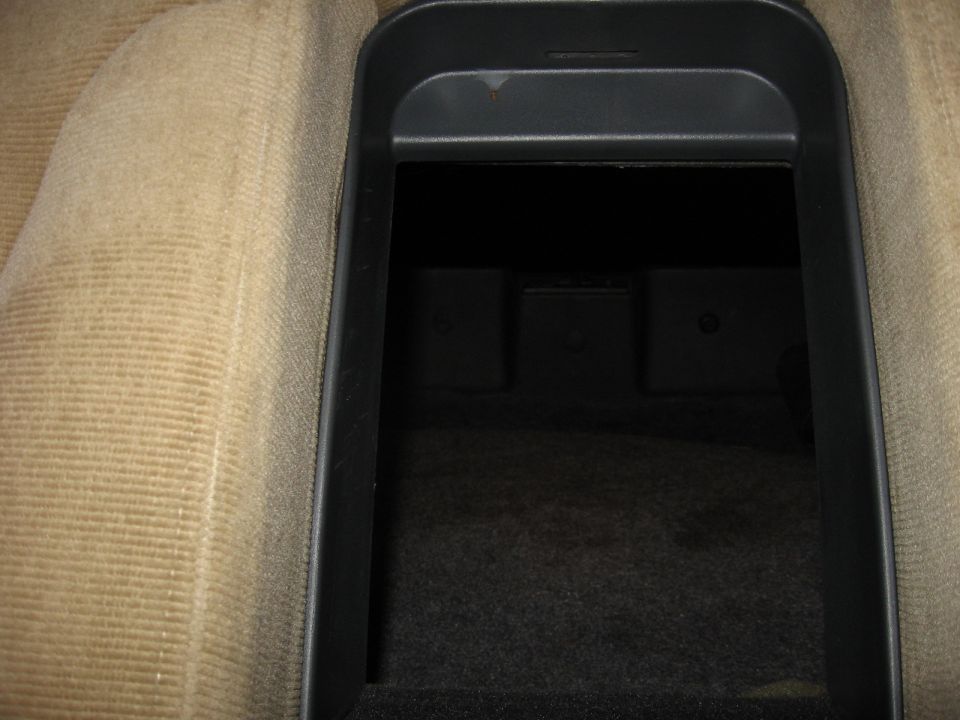 Car interior shot of an open center console storage bin with tan fabric seats visible to the left