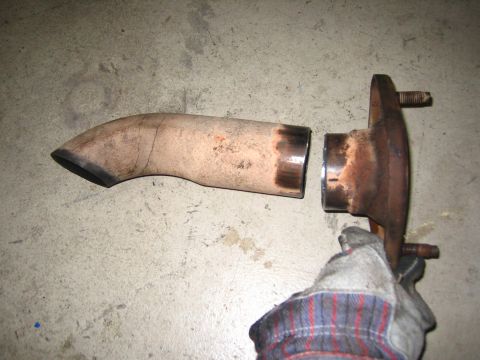 2001 Jeep Wrangler - A detached exhaust pipe and flange assembly lies on a concrete surface, held by a gloved hand.