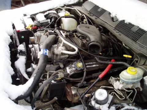 2000 Ford E350 - The engine bay of a vehicle is covered in snow, highlighting various mechanical parts.