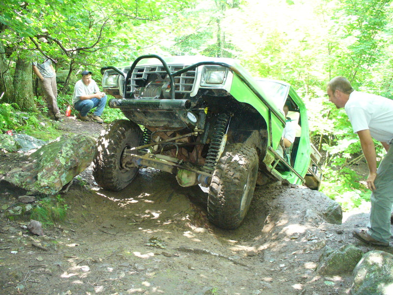 Green lifted Ford 4x4 crawling over rocks on a forest trail with spectators