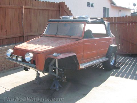 1990 Ford Bronco - Front view of a primer-orange Volkswagen Thing raised on jack stands, fitted with auxiliary driving lights on the front bumper.