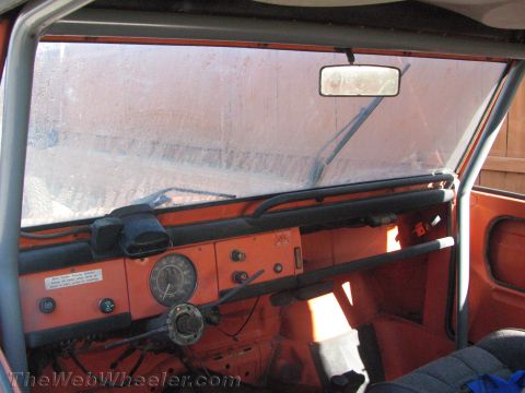 1990 Ford Bronco - Interior view of an orange Volkswagen Thing showing the flat painted metal dash, round gauge, and a roll bar across the cabin.