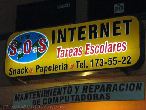 1990 Ford Bronco - lit yellow business sign for S.O.S Internet advertising Tareas Escolares, snacks, and stationery, with a phone number, at night.