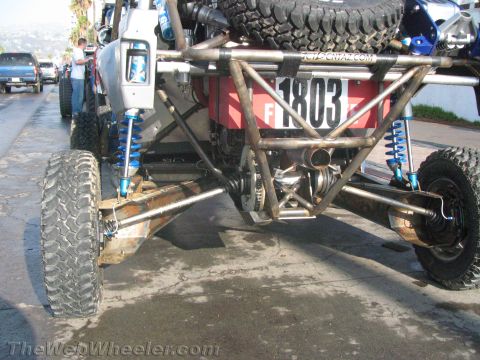 1990 Ford Bronco - Low rear view of a tube-frame race buggy numbered 1803 exposing its rear axle, halfshafts, exhaust, and blue coilover shocks.