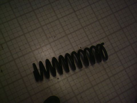 2001 Dodge 2500 - A single black coil spring is shown lying on a grid-patterned floor.