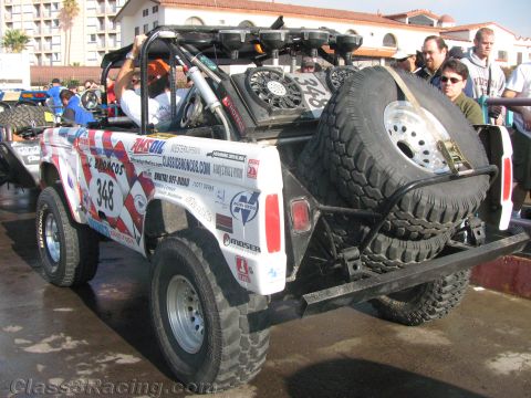 1990 Ford Bronco - Rear three-quarter view of a white and red early Bronco off-road racer #348 with a rear-mounted spare tire and Classic Broncos livery.