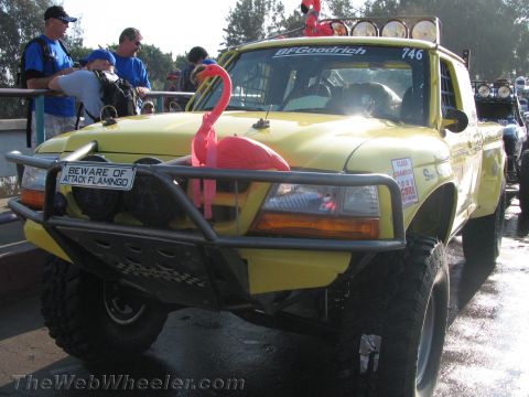 1990 Ford Bronco - Front three-quarter view of a lifted yellow off-road race truck #746 sporting a pink flamingo and a Beware of Attack Flamingo plate.