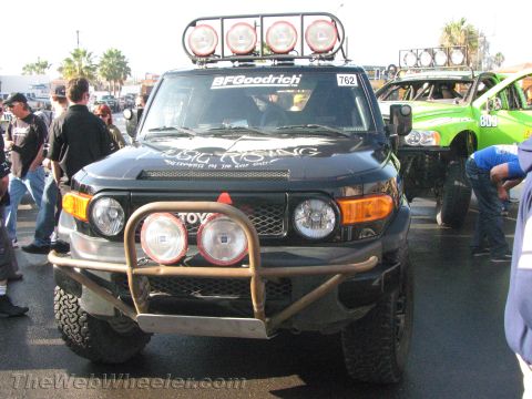 1990 Ford Bronco - Front view of a black Toyota FJ Cruiser off-road racer #762 with a four-light roof bar and tubular front bumper in a crowded staging area.