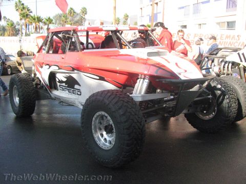 1990 Ford Bronco - Front three-quarter view of a red and silver tube-chassis off-road race buggy with SPEED graphics on big mud tires.