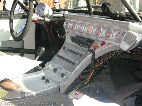1990 Ford Bronco - Interior of an off-road race truck cockpit showing the steering wheel, a row of gauges, an aluminum switch panel and a two-way radio.