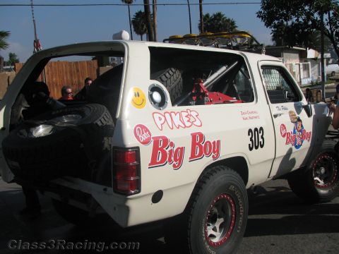 1990 Ford Bronco - Rear three-quarter view of a white off-road race SUV #303 wearing Bob's Big Boy graphics and a smiley face decal, with a spare tire.