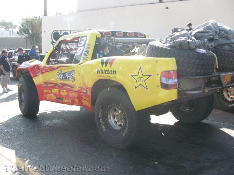 1990 Ford Bronco - yellow off-road race truck, number 39, sits in a paved staging area showing red flames, a Rockstar star logo and a rear-mounted spare tire.