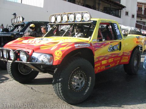 1990 Ford Bronco - front of a yellow flame-painted off-road race truck, number 39, with a roof-mounted light bar and many sponsor decals at a staging area.