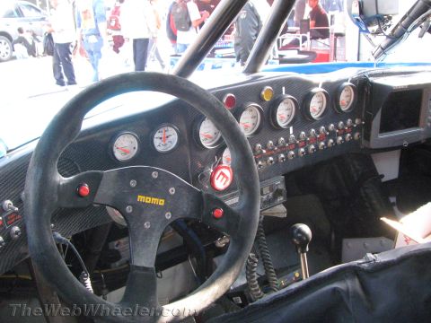 1990 Ford Bronco - cockpit of a race vehicle showing a black MOMO suede steering wheel, carbon-fiber dash, multiple gauges and toggle switches.
