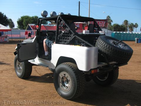 1990 Ford Bronco - white open-top FJ-style 4x4 with a roll cage, roof light bar and rear spare tire sits on dirt with Tecate banners behind.
