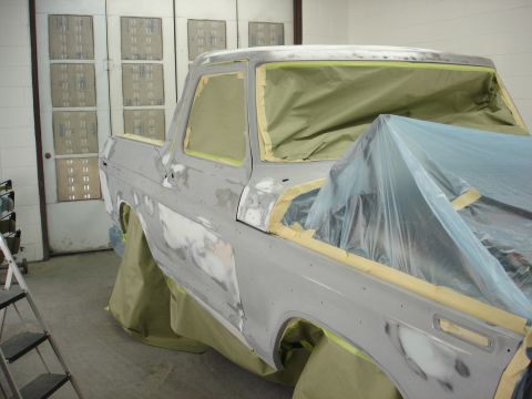 1979 Ford Bronco - A Ford truck body is covered in masking tape and plastic in a workshop, ready for paint.