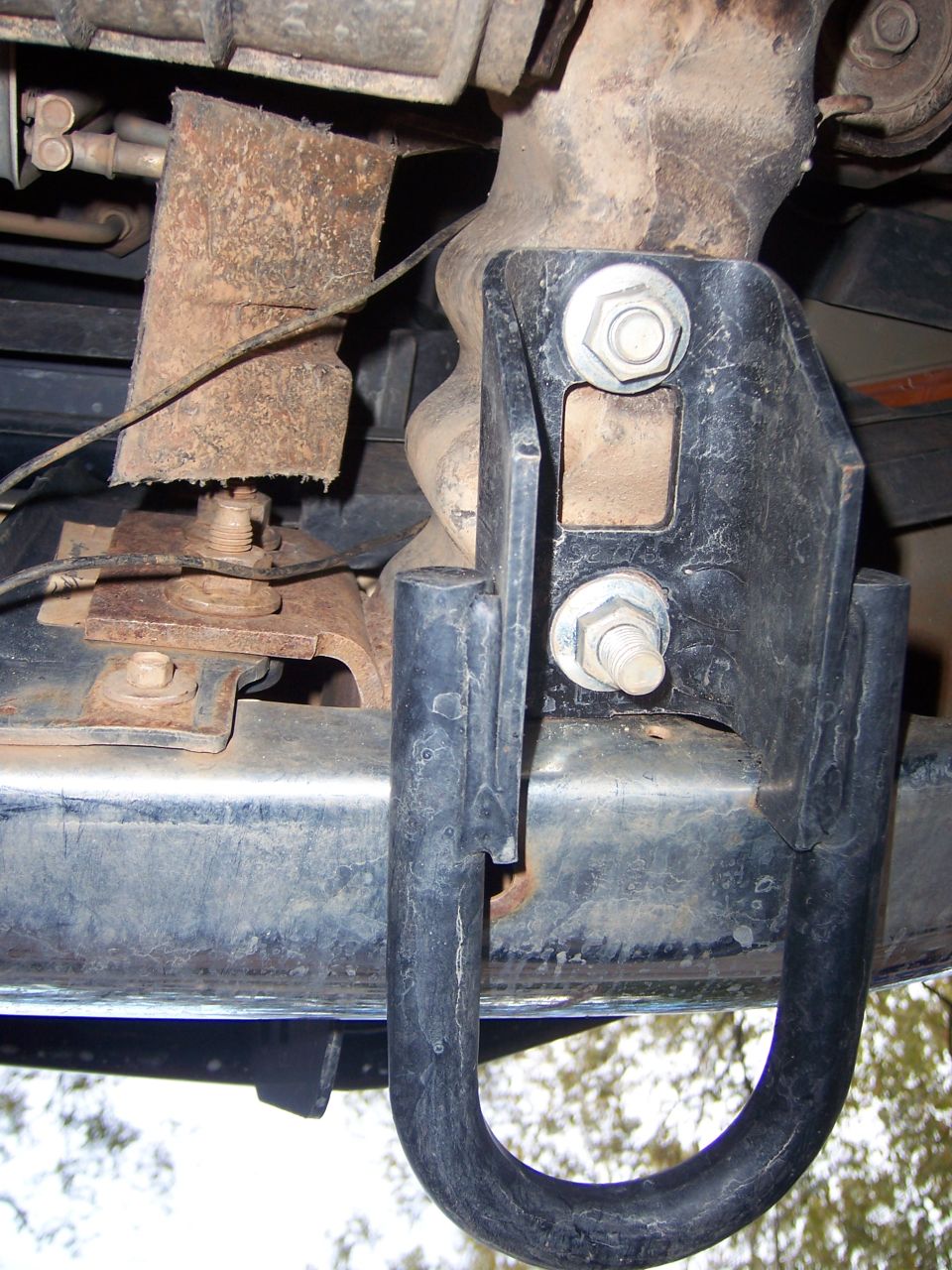 Close-up of a vehicle's undercarriage showing a tow hitch attached to the frame. Some rust is visible on other components