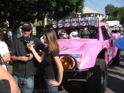 1990 Ford Bronco - man and woman conduct an interview in front of a pink off-road race truck topped with a roof-mounted light bar.