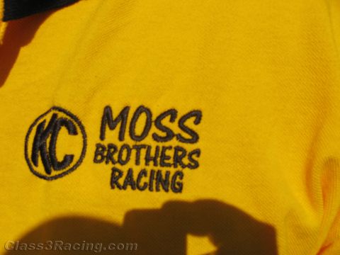 1990 Ford Bronco - Close-up of a yellow shirt embroidered with a circular KC logo and the words Moss Brothers Racing.