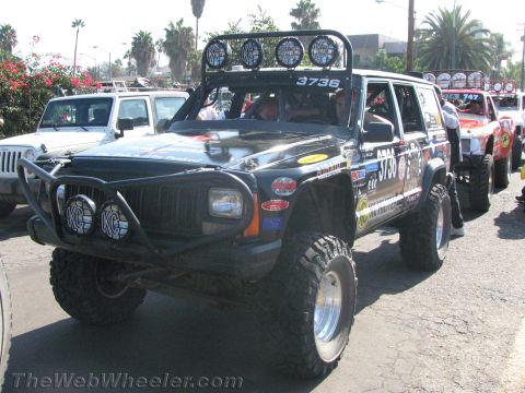 1990 Ford Bronco - black lifted Jeep Cherokee off-road racer number 3736 with a front brush bar and roof light bar at a staging area.