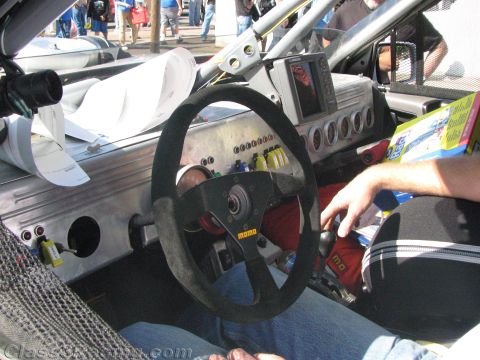 1990 Ford Bronco - Interior of a race car showing a suede MOMO steering wheel, shifter and a metal dash with toggle switches and gauges.
