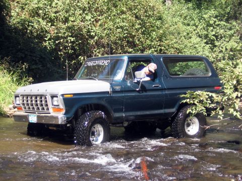 1979 Ford Bronco - A Ford Bronco navigates a rocky stream surrounded by lush green foliage.