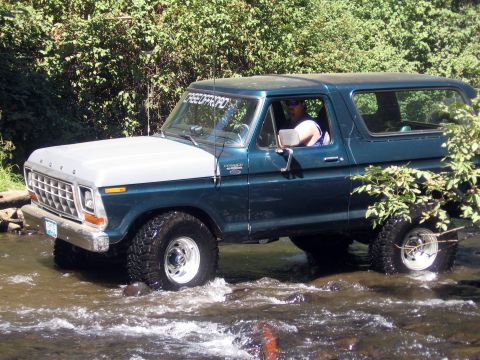 1979 Ford Bronco - A teal and silver 1979 Ford Bronco navigates a rocky stream, with a "CREEDOFFROAD.COM" sticker visible on the windshield.