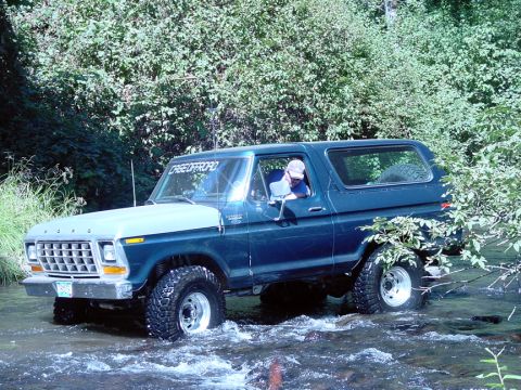 1979 Ford Bronco - A Ford Bronco navigates a rocky stream surrounded by dense foliage.