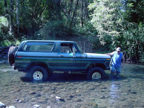 1979 Ford Bronco - A man stands beside a dark green Ford Bronco as it sits in a rocky, shallow stream surrounded by trees.
